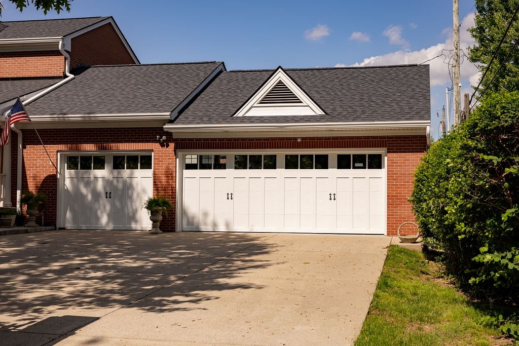 A brick house with a dark grey shingle roof and white garage doors