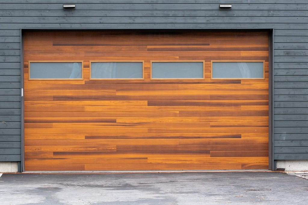 A modern brown faux wooden exterior garage door with four small horizontal glass windows