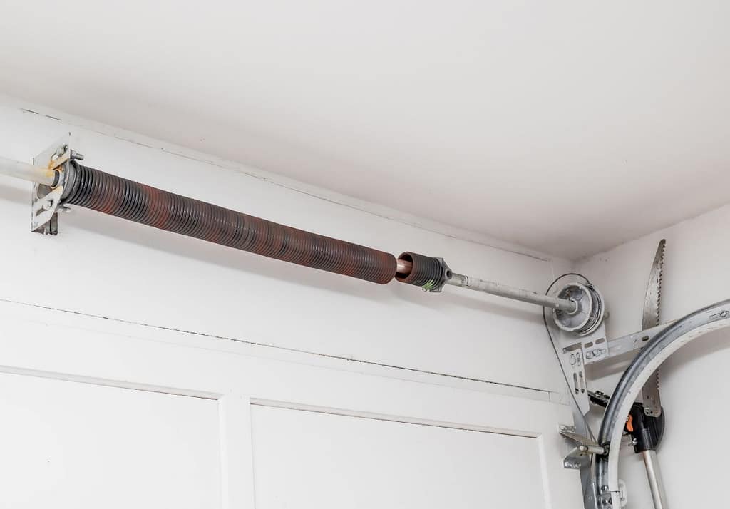 Garage door spring replacement closeup torsion spring inside house with white walls