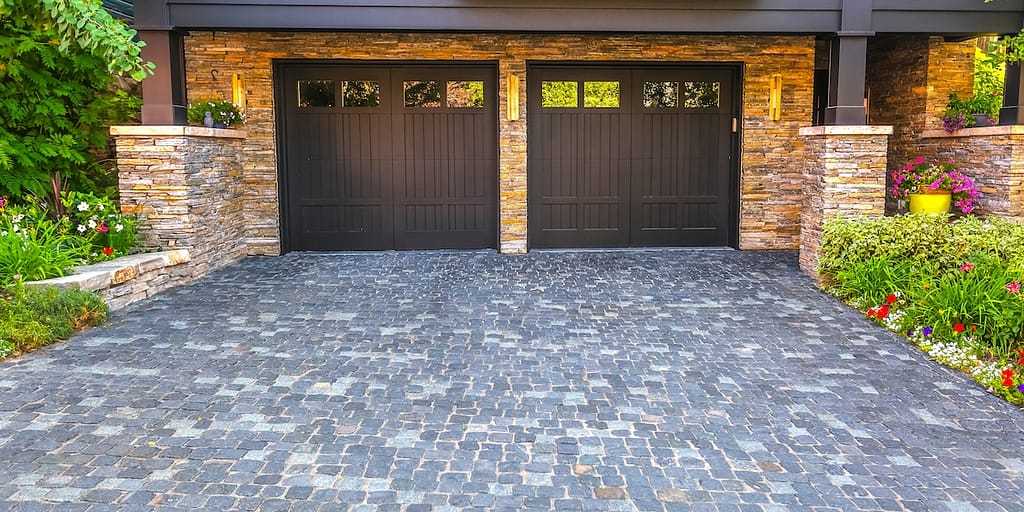 Two dark brown garage doors are set in a stone facade