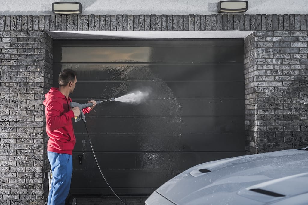 A man in a red hoodie uses a pressure washer for garage door cleaning