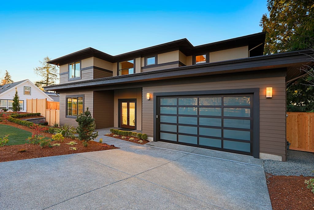New construction home exterior with contemporary house plan features low slope roof, brown siding and glass garage door.