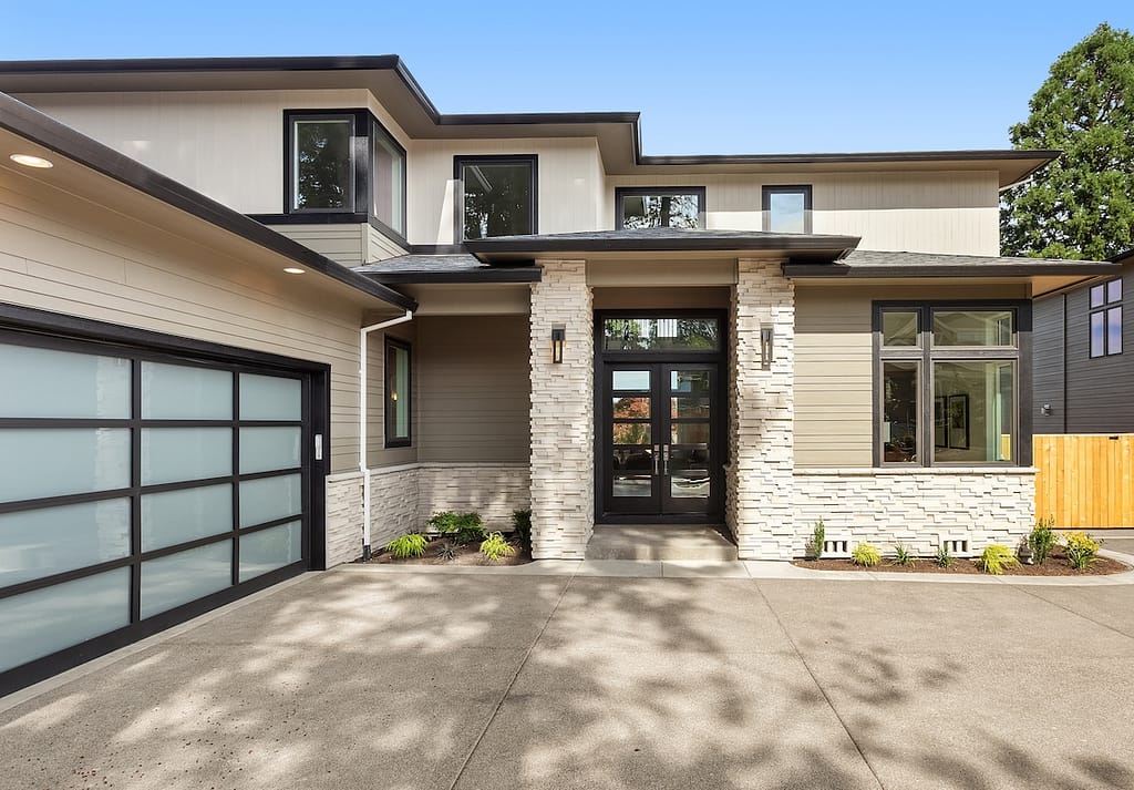 Beautiful modern luxury home exterior on bright sunny day with blue sky. Features columns flanking entrance and modern garage door with glass panels.
