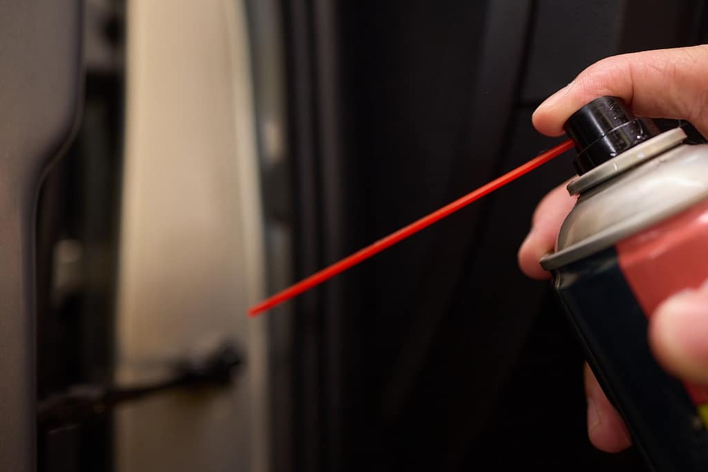 Spray lubricant on car door hinges for smooth operation and preventing corrosion for optimal functionality