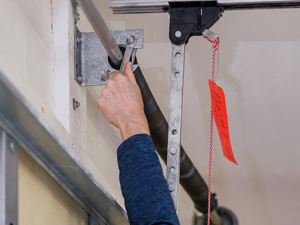 Man repairing electric garage door coiled tension spring.